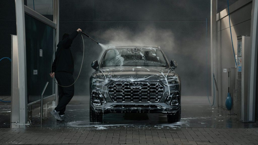 Người cầm vòi xịt nước lên chiếc xe SUV đen đứng giữa khoang rửa mờ hơi nước